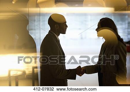 Stock Image - Businessman and businesswoman handshaking in lobby. Fotosearch