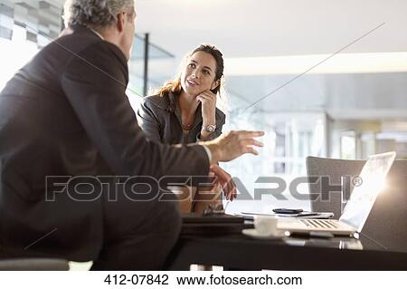 Stock Image - Businessman and businesswoman talking in lobby. Fotosearch