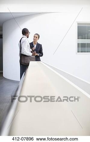 Stock Photograph - Businessman and businesswoman talking in office corridor. Fotosearch