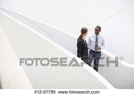 Stock Photography - Businessman and businesswoman talking on modern staircase. Fotosearch