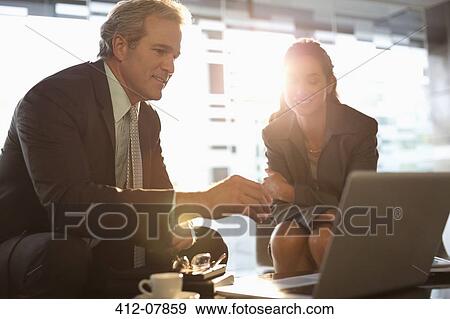 Stock Photo - Businessman and businesswoman using laptop in lobby. Fotosearch