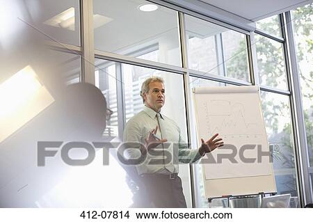 Businessman gesturing at flipchart in meeting View Large Photo Image Picture - Businessman gesturing at flipchart in meeting. Fotosearch