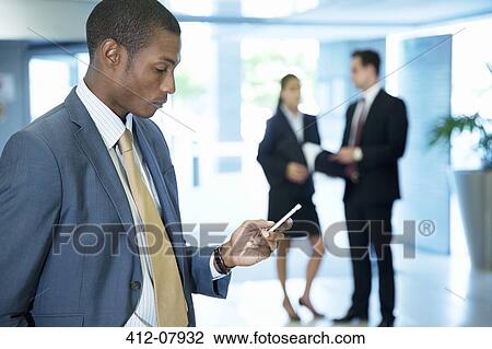Businessman text messaging with cell phone in lobby View Large Photo Image Stock Image - Businessman text messaging with cell phone in lobby. Fotosearch