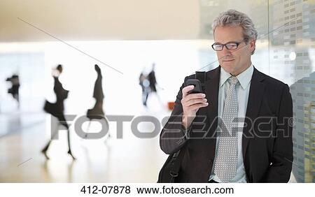 Stock Photo - Businessman text messaging with cell phone in lobby. Fotosearch
