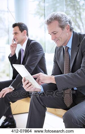 Businessman using digital tablet in lobby View Large Photo Image Picture - Businessman using digital tablet in lobby. Fotosearch