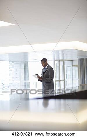 Stock Image - Businessman using digital tablet in lobby. Fotosearch
