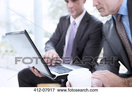 Businessmen drinking coffee and sharing laptop View Large Photo Image Stock Photo - Businessmen drinking coffee and sharing laptop. Fotosearch