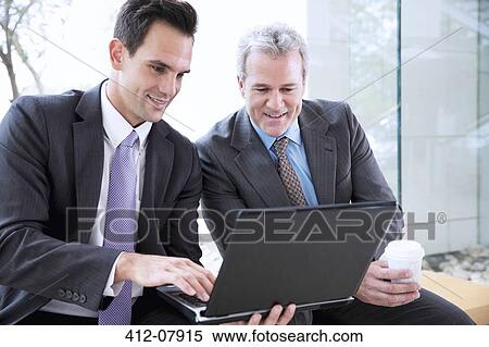 Businessmen drinking coffee and sharing laptop View Large Photo Image Stock Photography - Businessmen drinking coffee and sharing laptop. Fotosearch