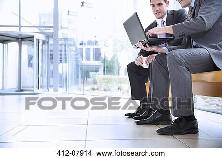 Businessmen sharing laptop in lobby View Large Photo Image Picture - Businessmen sharing laptop in lobby. Fotosearch