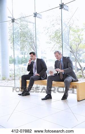 Businessmen using cell phone and digital tablet in lobby View Large Photo Image Stock Image - Businessmen using cell phone and digital tablet in lobby. Fotosearch