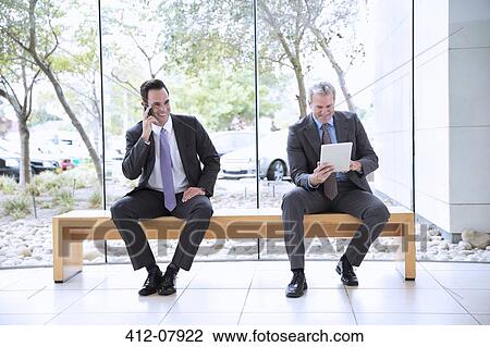 Businessmen using cell phone and digital tablet in lobby View Large Photo Image Stock Image - Businessmen using cell phone and digital tablet in lobby. Fotosearch