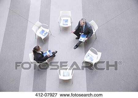 Stock Photo - High angle view of businessman and businesswoman talking at chairs in circle. Fotosearch