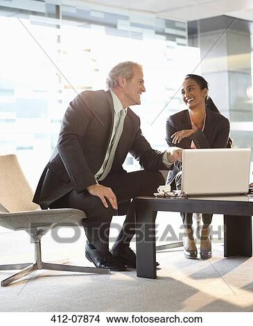 Smiling businessman and businesswoman using laptop in lobby View Large Photo Image Picture - Smiling businessman and businesswoman using laptop in lobby. Fotosearch