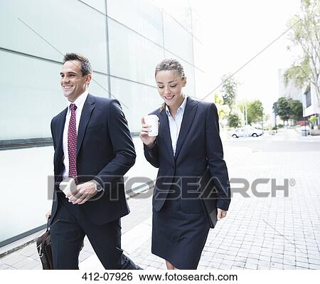 Smiling businessman and businesswoman walking with coffee View Large Photo Image Stock Photograph - Smiling businessman and businesswoman walking with coffee. Fotosearch