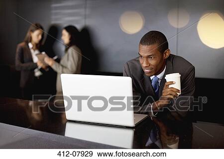 Stock Photo - Smiling businessman drinking coffee and using laptop. Fotosearch