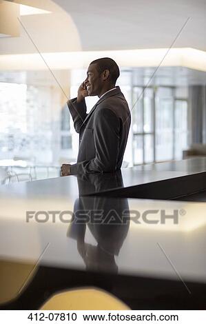 Stock Image - Smiling businessman talking on cell phone in lobby. Fotosearch