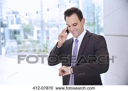 Smiling businessman talking on cell phone and looking at wristwatch View Large Photo Image Stock Image - Smiling businessman talking on cell phone and looking at wristwatch. Fotosearch