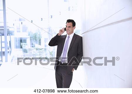 Stock Photo - Smiling businessman talking on cell phone in lobby. Fotosearch