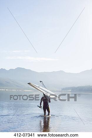 Stock Image - Man carrying rowing scull into lake. Fotosearch