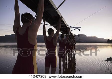 Rowing team carrying boat overhead into lake View Large Photo Image Stock Photo - Rowing team carrying boat overhead into lake. Fotosearch