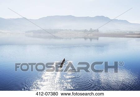 Stock Image - Rowing team rowing scull on lake. Fotosearch