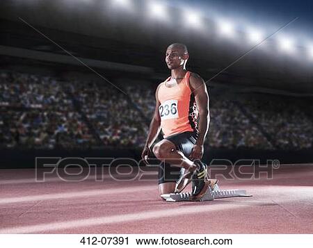 Stock Image - Runner with feet in starting block on track. Fotosearch