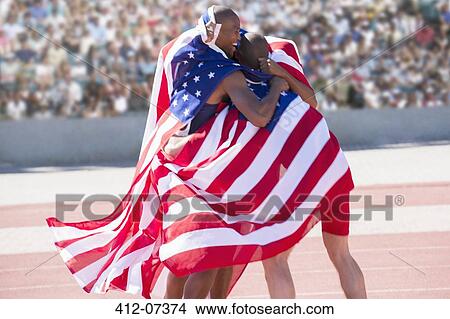 Picture - Track and field athletes wrapped in American flag on track. Fotosearch