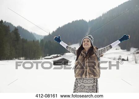 Stock Image - Carefree woman with arms outstretched in snowy field. Fotosearch