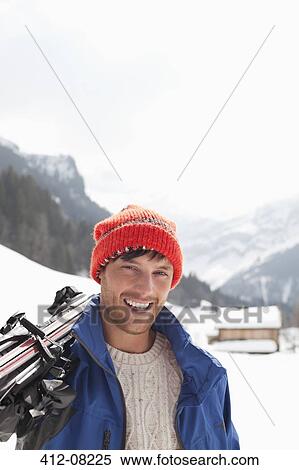 Stock Photography - Close up portrait of smiling man carrying skis in snowy field. Fotosearch