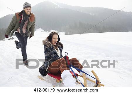 Enthusiastic couple sledding in snowy field View Large Photo Image Stock Photo - Enthusiastic couple sledding in snowy field. Fotosearch