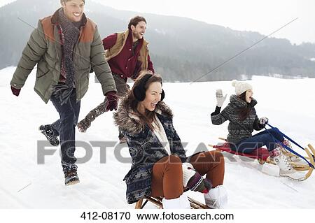Enthusiastic friends sledding in snowy field View Large Photo Image Stock Image - Enthusiastic friends sledding in snowy field. Fotosearch