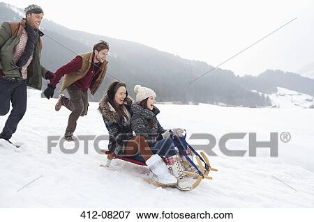 Stock Photo - Enthusiastic friends sledding in snowy field. Fotosearch
