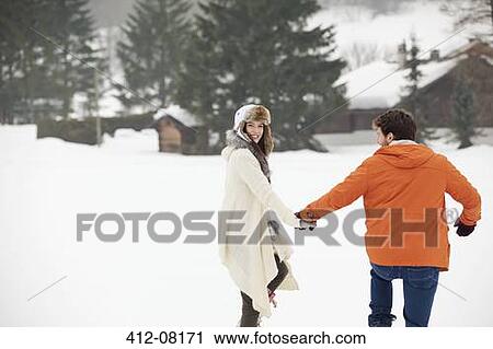 Stock Image - Happy couple holding hands and walking in snowy field. Fotosearch