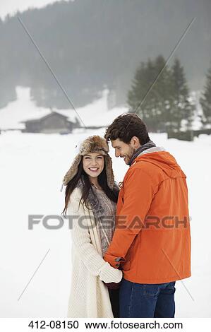 Stock Image - Happy couple holding hands in snowy field. Fotosearch