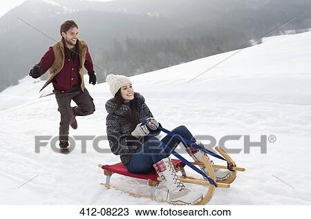 Happy couple sledding in snowy field View Large Photo Image Stock Image - Happy couple sledding in snowy field. Fotosearch