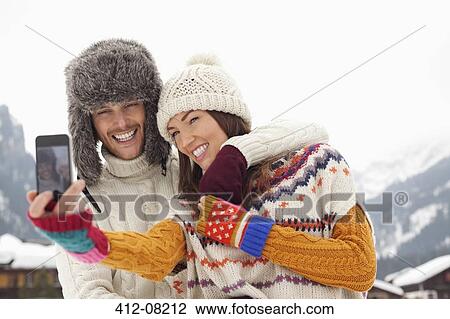 Stock Image - Happy couple taking self-portrait with camera phone near mountains. Fotosearch