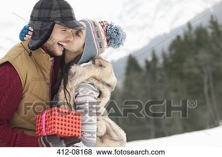 Happy couple with Christmas gift kissing in snowy field View Large Photo Image Stock Photo - Happy couple with Christmas gift kissing in snowy field. Fotosearch