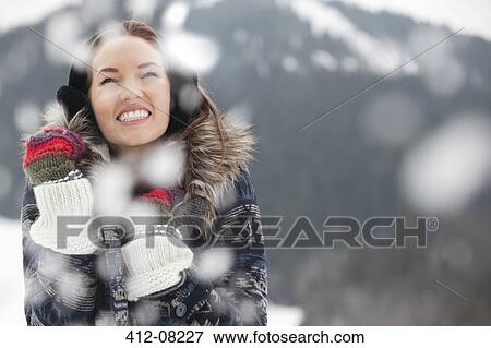 Stock Photo - Happy woman wearing ear muffs and gloves in snow. Fotosearch