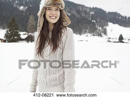 Stock Image - Happy woman wearing fur hat in snowy field. Fotosearch