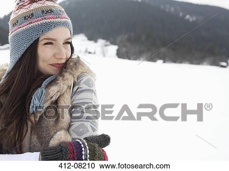 Stock Image - Happy woman wearing knit hat and gloves in snowy field. Fotosearch