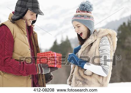 Stock Photo - Man surprising woman with gift in snowy field. Fotosearch