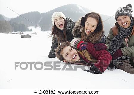 Stock Image - Playful friends laying in snowy field. Fotosearch
