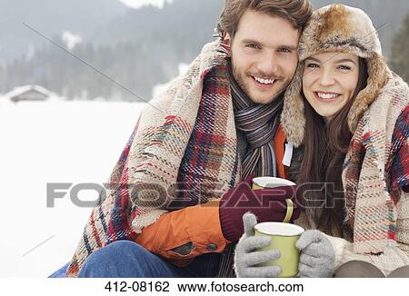 Stock Image - Portrait of happy couple drinking coffee in snowy field. Fotosearch
