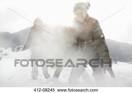 Stock Photography - Portrait of playful friends enjoying snowball fight in field. Fotosearch