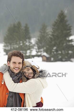Stock Photograph - Portrait of smiling couple hugging in snowy field. Fotosearch