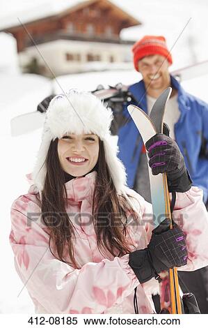 Stock Photography - Portrait of smiling couple with skis outside cabin. Fotosearch
