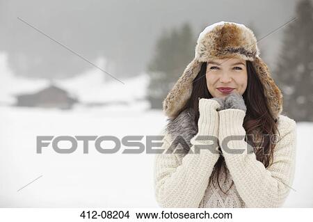 Picture - Portrait of smiling woman wearing fur hat and gloves in snowy field. Fotosearch