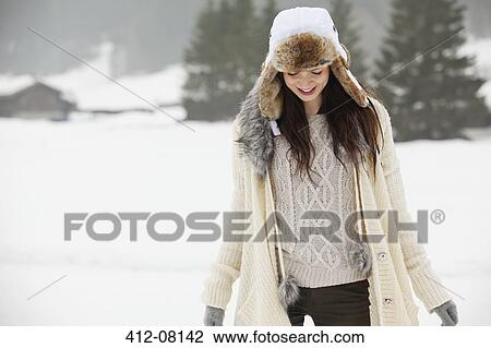 Stock Image - Smiling woman wearing fur hat in snowy field. Fotosearch