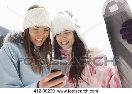 Stock Photo - Women with skis text messaging with cell phone. Fotosearch