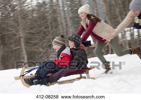 Stock Photo - Enthusiastic family sledding in snowy field. Fotosearch